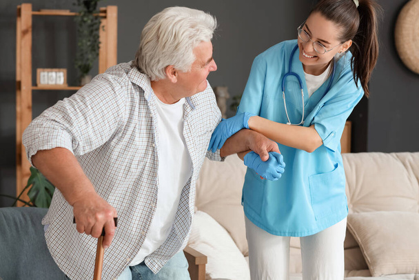 Infirmière aidant l'homme âgé avec bâton à se lever du fauteuil à la maison - Photo, image