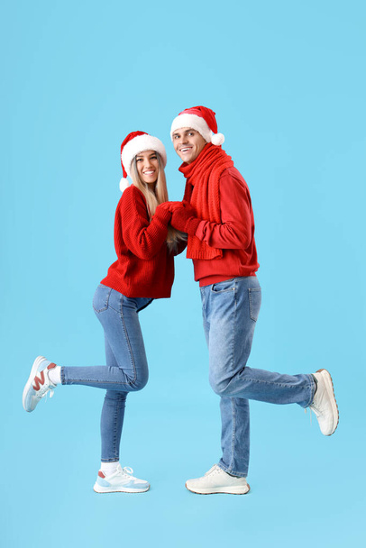Счастливая молодая пара в шляпах Санты, держась за руки на синем фоне - Фото, изображение