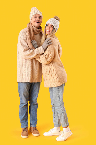 Happy young couple in winter clothes hugging on yellow background - Photo, Image