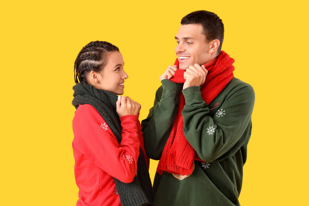 Sarı arka planda eşarpları olan Noel süveteri giyen genç bir çift. - Fotoğraf, Görsel