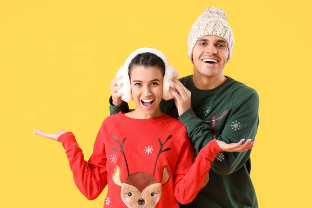 Fiatal pár karácsonyi pulóverek sárga háttér - Fotó, kép