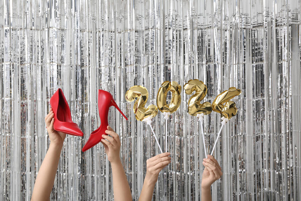 Női kéz magas sarkú cipő és ábra 2024 készült léggömbök ezüst tinsel háttér - Fotó, kép