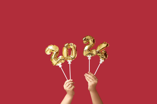 Vrouwelijke handen met figuur 2024 gemaakt van ballonnen op rode achtergrond - Foto, afbeelding