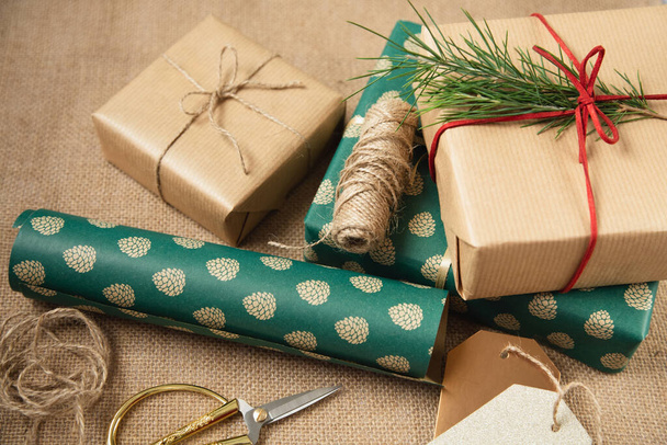 Prezenty zapakowane w Boże Narodzenie piękny papier, nożyczki i osobiste znaczniki prezentów są na tle płótna. Przygotowanie do świąt. - Zdjęcie, obraz