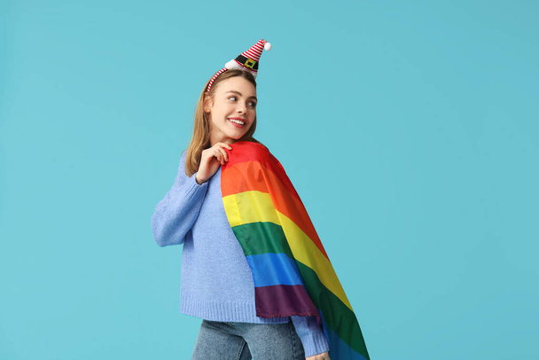 Молодая женщина в шляпе Санты с флагом ЛГБТ на синем фоне - Фото, изображение
