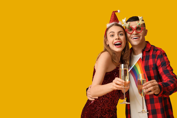 Sarı arka planda LGBT bayrağı ve şampanya taşıyan genç bir çift. - Fotoğraf, Görsel