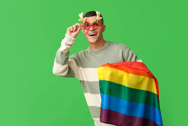 Jonge man in kerstbril met LGBT vlag op groene achtergrond - Foto, afbeelding