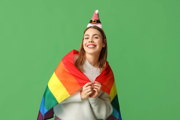 Молода жінка в капелюсі Санта з прапором ЛГБТ на зеленому фоні - Фото, зображення