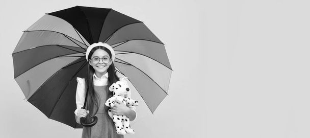 happy teen girl under colorful umbrella in autumn season hold toy. Child with autumn umbrella, rainy weather, horizontal poster, banner with copy space - Foto, imagen