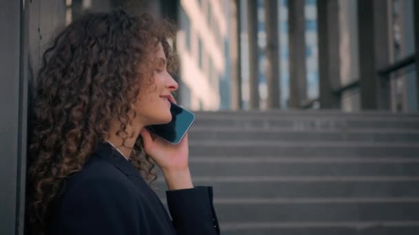 Кавказька бізнес-леді роботодавець жінка-менеджер дівчина розмовляє смартфоном біля офісної будівлі стіни за межами молодої ділової жінки-підприємниці обговорювати телефонні розмови з клієнтом на відкритому повітрі мобільні розмови - Кадри, відео