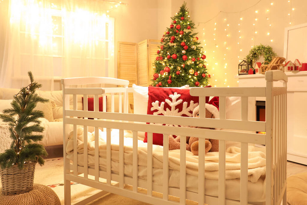 Interior del dormitorio con cuna, árboles de Navidad y luces brillantes en la noche - Foto, Imagen