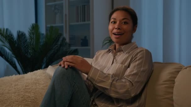 Meglepett megdöbbent boldog afro-amerikai nő etnikai lány lakástulajdonos a kanapén este otthon nézi kamera csoda meglepett öröm öröm jó hír győzelem ajánlat lehetőséget mondani wow elképesztő - Felvétel, videó