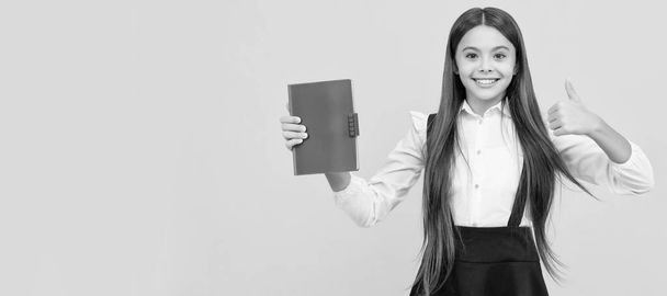 Счастливая девочка в школьной форме предлагает книгу, большой палец вверх. Портрет школьницы, заголовок баннера студии. Лицо школьника, копирайт - Фото, изображение