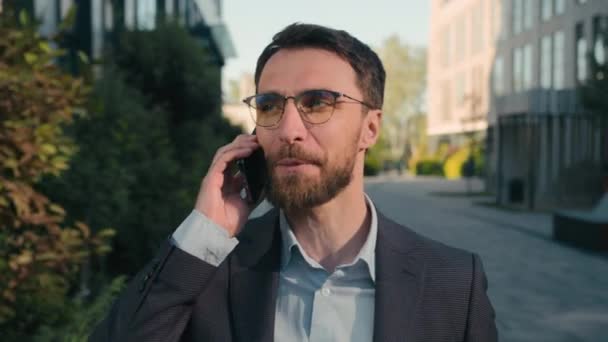 Boldog mosolygós kaukázusi férfi beszél mobiltelefon séta szabadban nevetés beszél mobiltelefon vidám mosoly barátságos chat üzletember beszélgetés kívül smartphone hívás üzleti munka a városban - Felvétel, videó