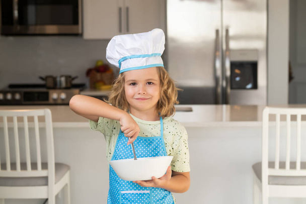 Kinderkoch kochen mit Kochplatte. Kinderkoch mit Kochmütze bereitet Essen in der Küche zu. Kind macht lecker. Mahlzeit zubereiten - Foto, Bild