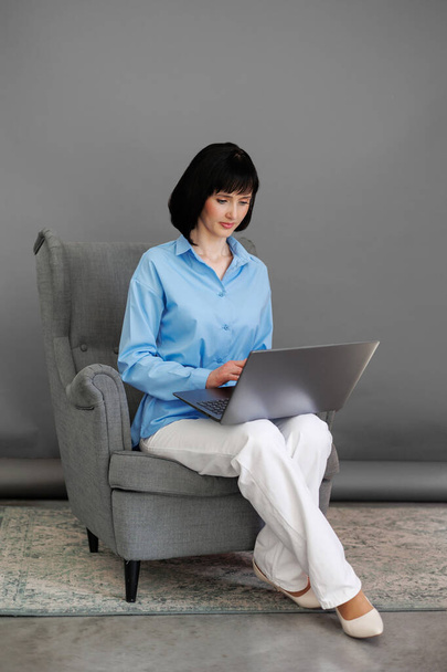 Positive adult business woman mentor teacher psychologist sits on armchair consulates talk in online seminar on laptop,work with patients at home in remote, teach advice by digital training at office. - Photo, Image