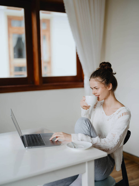 Mujer joven creativa que trabaja en un escritorio en casa en un interior acogedor con una taza de bebida, freelancer oficina en casa con una sonrisa, la comunicación y la educación en línea. Foto de alta calidad - Foto, imagen