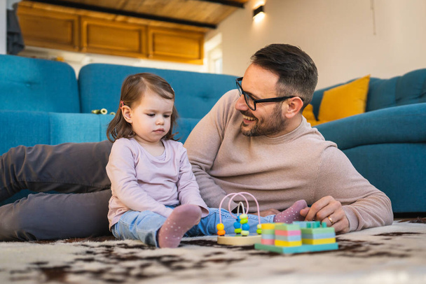 Apa és lánya játszani a padlón otthon érett felnőtt kaukázusi férfi játszani az ő két éves gyermek kisbaba lány szórakozás nevelés és kötődés családi idő koncepció másolja tér valós emberek - Fotó, kép