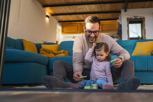 Батько і дочка грають на підлозі вдома зрілий дорослий кавказький чоловік грає зі своєю дворічною дитиною маленькою дівчинкою, яка веселиться батьківством і зв'язує концепцію сімейного часу копіювання простору справжніми людьми
 - Фото, зображення