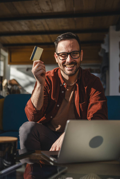 Yksi mies aikuinen kypsä valkoihoinen mies istuu kotona onnellinen hymy kannettava tietokone pidä pankki luottokortti verkkokaupoissa ostaa internetissä käsite oikeita ihmisiä kopioi tilaa sähköisen kaupankäynnin pankkipalvelu - Valokuva, kuva