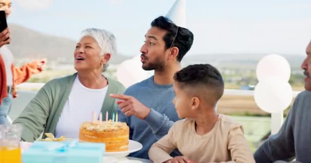 Communication, video call and big family at a birthday party celebration with a cake and presents. Happy, smile and people on virtual conversation with a phone to celebrate with man at outdoor event - Footage, Video