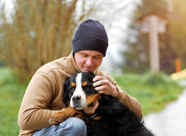 Un giovane lavora come addestratore di cani e abbraccia il suo bel cagnone carino di una razza di montagna bernese. Big Kind Dog ed è proprietario. Atmosfera pet-friendly. - Foto, immagini