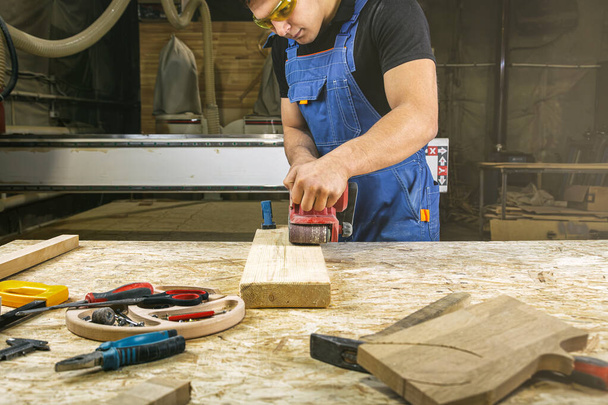 若い男ビルダーカーペンターのクローズアップは,ワークショップで木製ボードを磨きます - 写真・画像