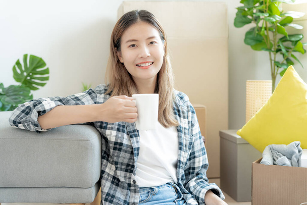 Moving house, relocation. asian woman feel good and recreation and drink coffee on new house, inside the room was a cardboard box containing personal belongings and furniture. move in condominium - Photo, Image