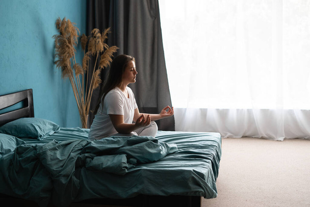 Ochtendmeditatie. Jonge ontspannen vrouw die yoga zen beoefent op bed nadat ze wakker werd. Kopieerruimte - Foto, afbeelding