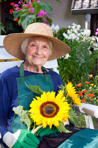 Senior vrouw op stoel bedrijf zonnebloemen - Foto, afbeelding