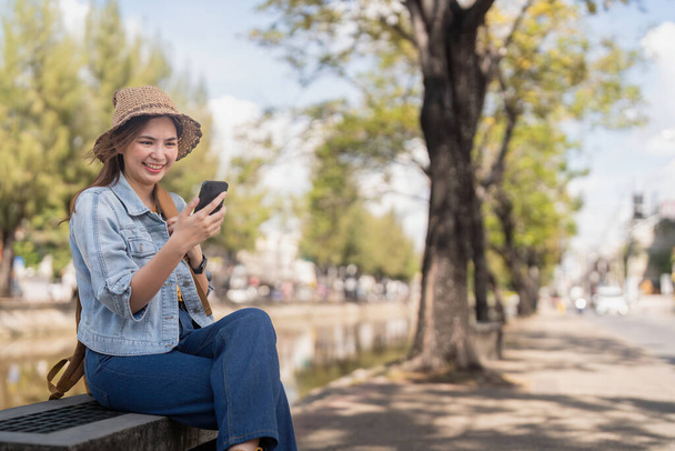 Genç, güzel, gülümseyen Asyalı kadın turist cep telefonu yönlendirmesini kullanıyor ya da sosyal medya kullanıyor.. - Fotoğraf, Görsel