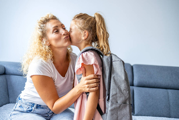 Nettes Mädchen mit Schulranzen küsst ihre Mutter, bevor sie zur Schule geht. - Foto, Bild