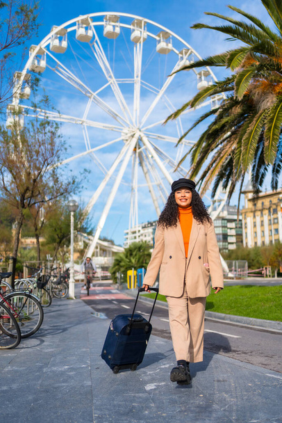 Vertical photo of a chic latin tourist arriving at a city with a Ferris wheel - Fotó, kép