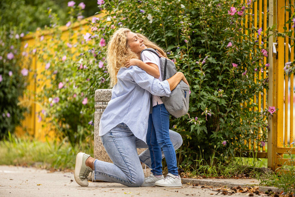 Moeder en dochter knuffelen elkaar voor de school. - Foto, afbeelding