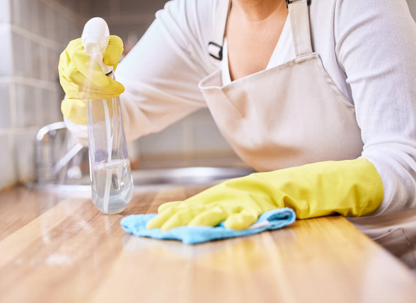 Γυναίκα, μπουκάλι ψεκασμού και τα χέρια καθαρισμού τραπέζι στο νοικοκυριό, υγιεινή ή απολύμανση με γάντια στην κουζίνα. Κλείσιμο της επιφάνειας σκουπίσματος, του μετρητή ή των επίπλων του θηλυκού προσώπου σε βακτήρια ή αφαίρεση μικροβίων. - Φωτογραφία, εικόνα