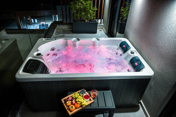 Relaks Whirlpool Bath: Rose Water Light Ambiance z płytą świeżych owoców w pobliżu. Idealny do przekazywania luksusowych i uspokajających doświadczeń kąpieli spa.  - Zdjęcie, obraz