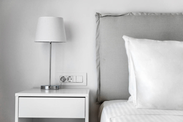 Concetto di camera da letto minimalista: Biancheria da letto bianca, cuscino e comodino con lampada. Perfetto per l'uso in pubblicazioni di arredamento domestico, concetti di interior design e promozioni stile di vita. - Foto, immagini