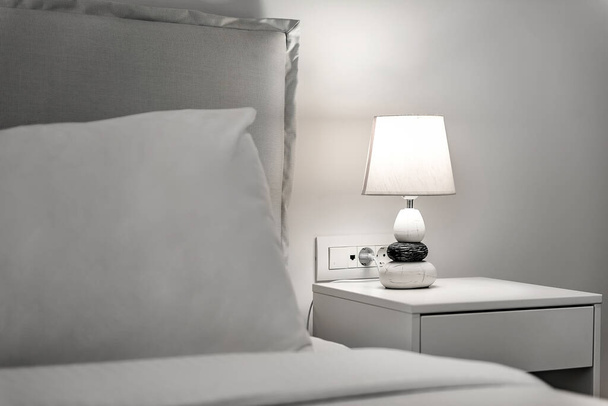 Minimalistický Ložnice koncepce: Bílé ložní prádlo, polštář a noční stolek s lampou. Ideální pro použití v domácí výzdobě publikací, koncepce interiérového designu a propagace životního stylu. - Fotografie, Obrázek