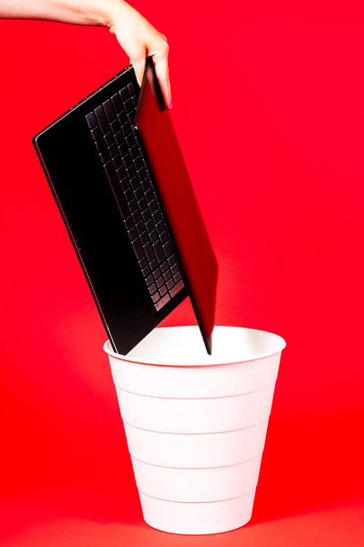 Black laptop in a trash bin on red background isolated - Photo, Image
