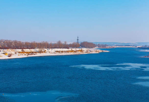Spokojny zimowy krajobraz z płynącą rzeką splata się w spokojnej scenerii dziewiczych, pokrytych śniegiem brzegów - Zdjęcie, obraz