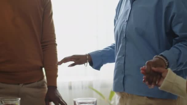 Colpo ritagliato di famiglia afroamericana in piedi intorno al tavolo da pranzo, tenendosi per mano e pregando prima di cena festiva a casa - Filmati, video