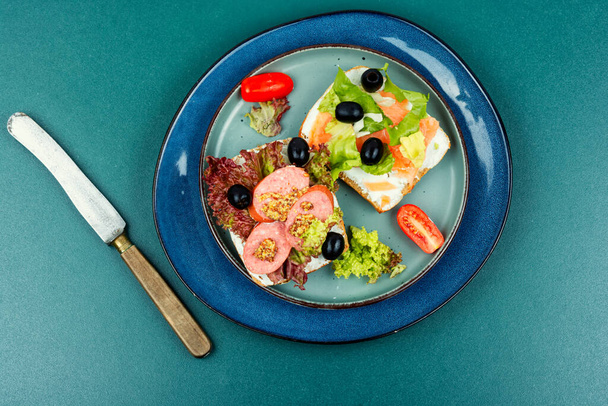 Смачні бутерброди з форелею та сосисками. Зерновий хліб, з вершковою сирною рибою та салямі, чорними оливками та салатом. Сніданок - Фото, зображення