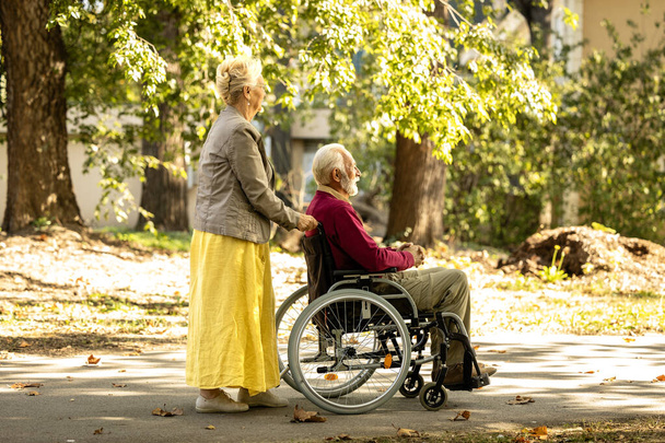 Mulher idosa empurrando cadeira de rodas com homem sênior em creche home park. - Foto, Imagem