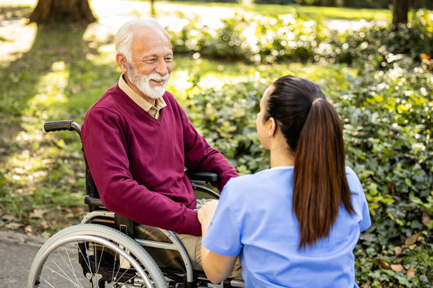 Assistante infirmière prenant soin d'un homme âgé en fauteuil roulant. - Photo, image