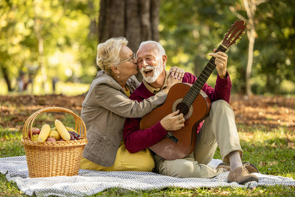 Couple de personnes âgées appréciant pique-niquer ensemble, jouer de la guitare et rire. Profiter de la retraite ensemble. - Photo, image