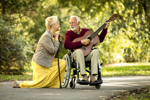 Coppia anziana amore e felicità. anziano uomo in sedia a rotelle suonare la chitarra per la sua bella moglie. - Foto, immagini