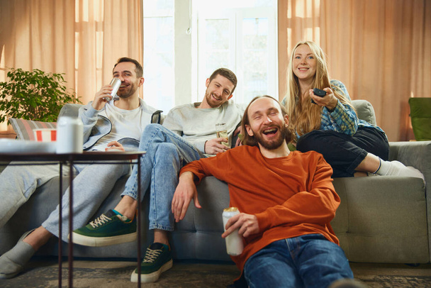 Blickwinkel auf eine fröhliche Gruppe von Freunden, die auf dem Sofa im Wohnzimmer sitzen und sich ein Fußballspiel, eine Meisterschaft, anschauen. Konzept der Freundschaft, Zweisamkeit, TV-Programm, Online-Event, Erholung. - Foto, Bild