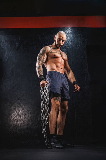 Un jeune homme de remise en forme debout dans la salle de gym et se préparant à la musculation avec une chaîne lourde. - Photo, image