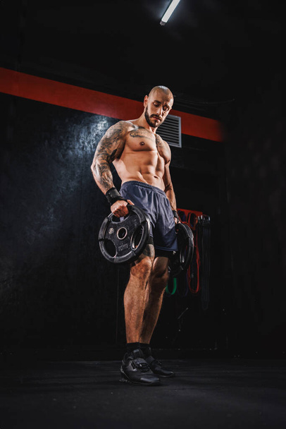 Tiro de um homem musculoso fitness jovem mostrando seus músculos perfeitos depois de trabalhar com placa de peso no ginásio. - Foto, Imagem