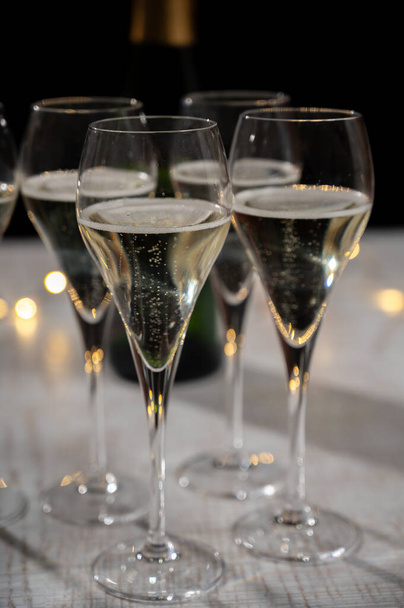 Fiesta de año nuevo, pequeñas burbujas de champán brut cava o vino prosecco en copas de tulipán con luces de guirnalda sobre fondo oscuro - Foto, imagen